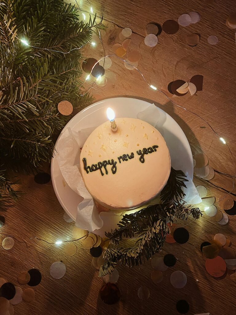 A New Year celebration cake with candle, decorations, and confetti in a cozy setting.