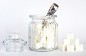 Close-up of a glass jar filled with sugar cubes on a white background. Minimalist stock photo.