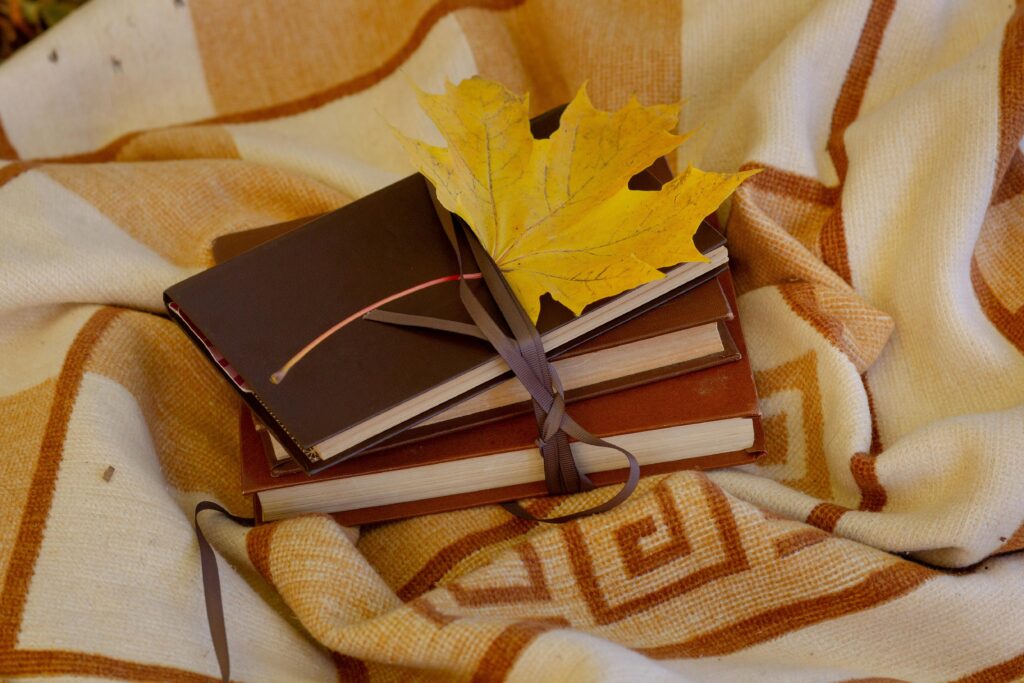 Autumn still life with books, a maple leaf, and a cozy blanket.