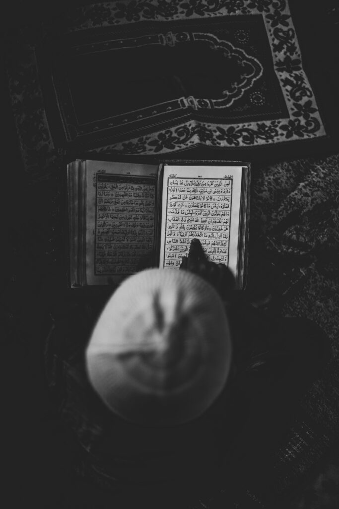 From above of unrecognizable person in hat sitting on rug and reading interesting thick book in retro fashioned room alone