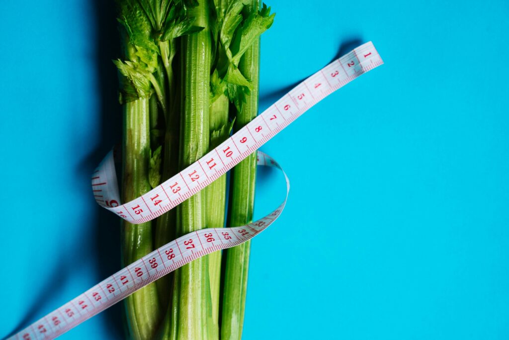 Close-up of celery stalks wrapped with measuring tape on a vibrant blue background, symbolizing health and diet.