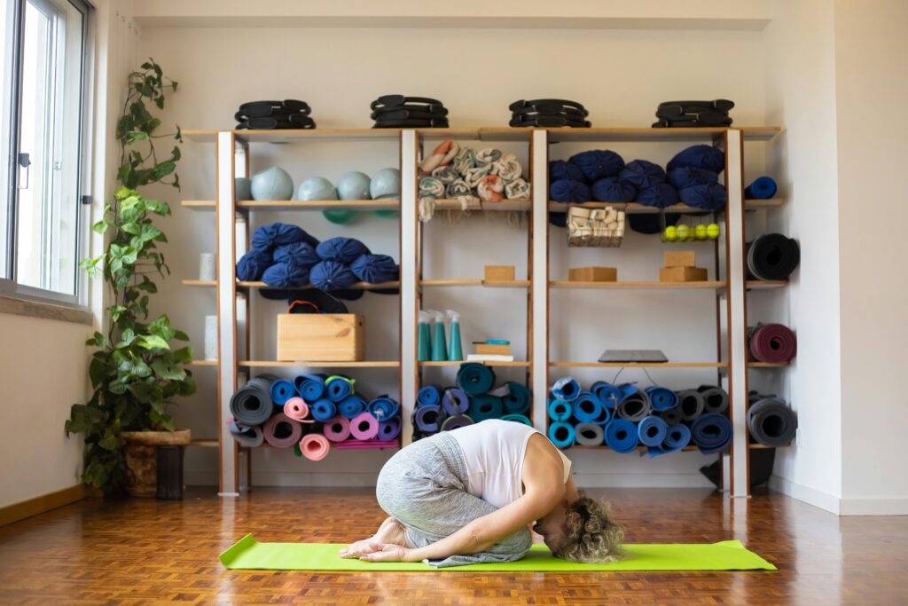 A woman performs yoga on a mat in a well-equipped studio, surrounded by props and natural light.