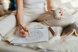 A woman enjoying a cozy moment with a coloring book and coffee in a bright, relaxed setting.