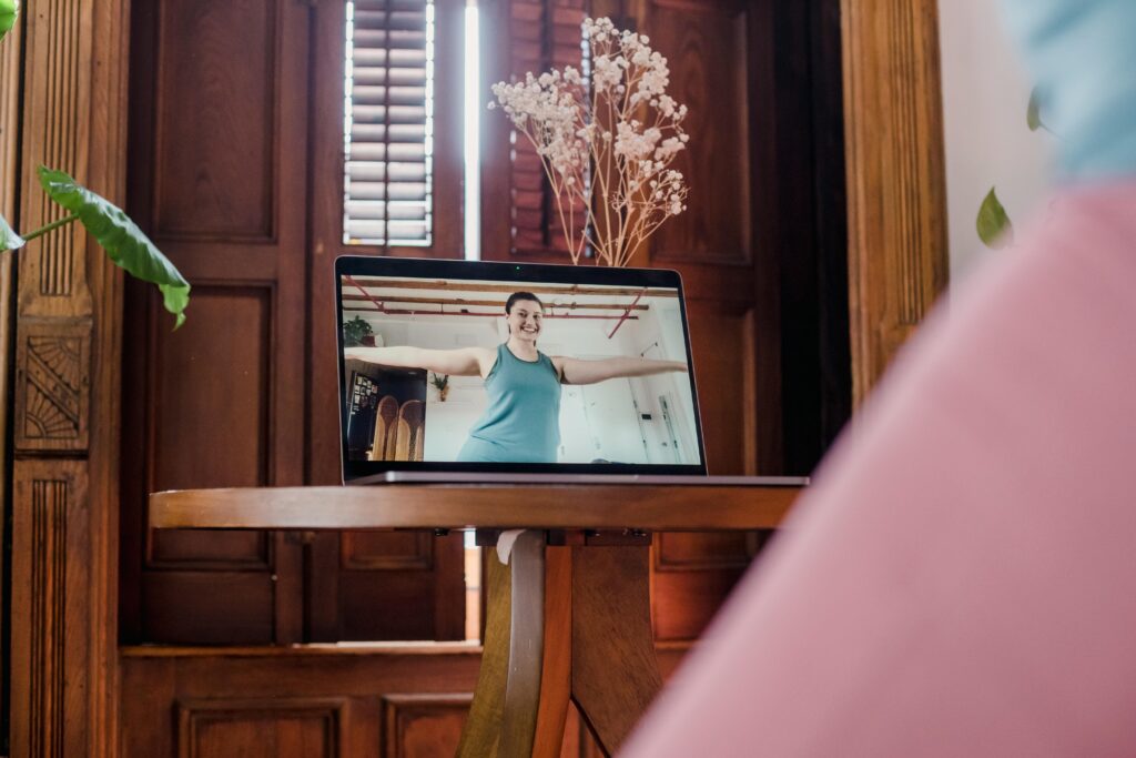 A woman engages in an online yoga session via laptop in a cozy home setting, focusing on wellness.