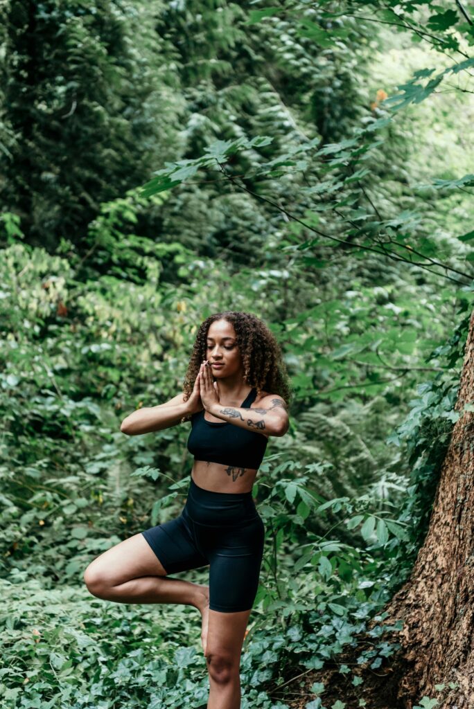 A woman in activewear practices yoga amidst lush green forest, embodying tranquility and mindfulness.