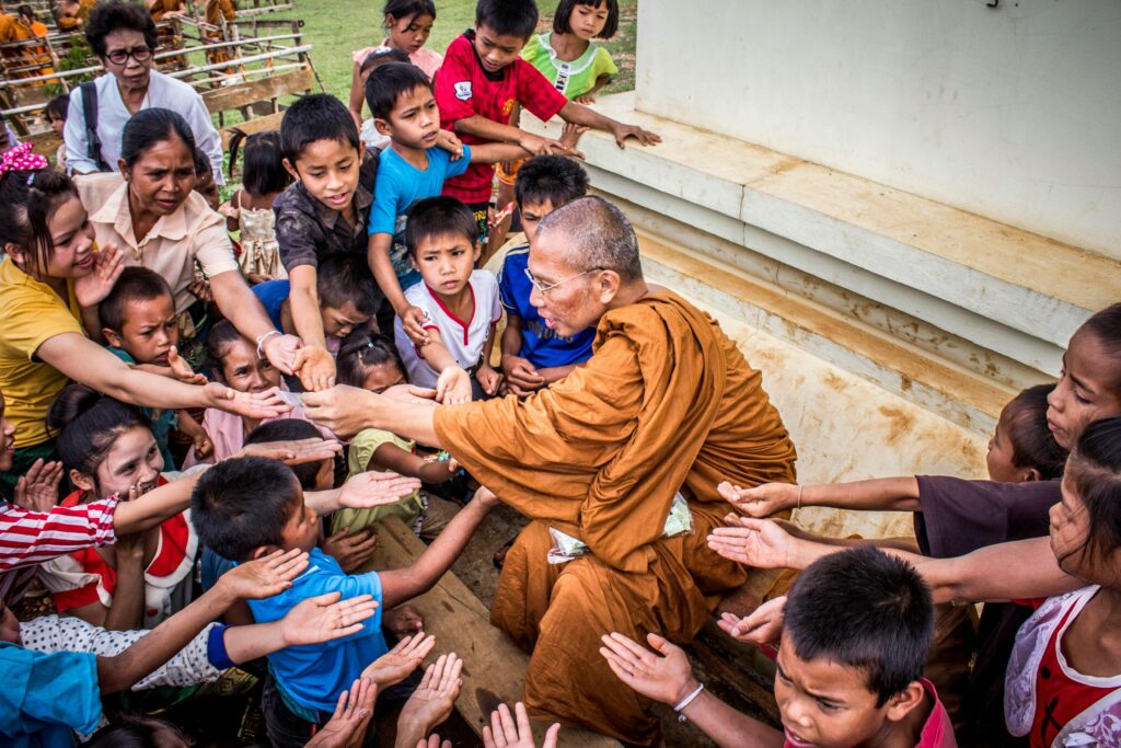 A Buddhist monk sharing gifts with children, capturing a moment of compassion and cultural tradition.
