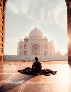A person meditates at sunrise facing the iconic Taj Mahal, capturing serenity and majesty.