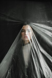 A striking portrait of a woman obscured by plastic, highlighting themes of pollution and feminism.