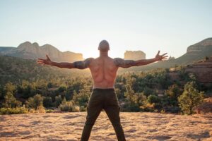 Back view of muscular male with naked torso doing Five Pointed Star pose while practicing yoga in nature at dawn
