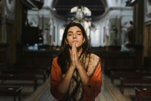A woman with closed eyes prays in a peaceful cathedral setting, conveying a sense of calm and spirituality.
