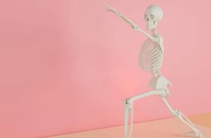 A skeleton model doing a yoga stretch on a pink backdrop, symbolizing fitness and anatomy.