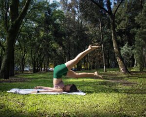 A woman performs a challenging yoga pose in a sunny park in Mexico City, promoting relaxation and fitness.