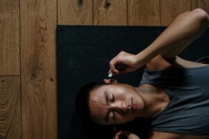 An Asian man relaxing with headphones, lying on a yoga mat in a serene indoor setting.