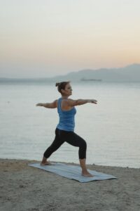 Woman performing Warrior 2 pose on the beach during twilight, combining fitness and tranquility.