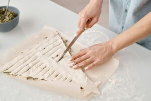 Close-up of hands slicing pastry dough in creative shape on kitchen counter.
