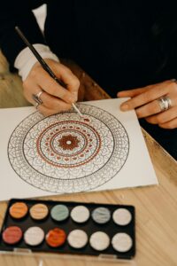 Close-up of hands painting a detailed mandala indoors, showcasing artistic creativity and precision.