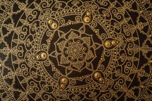 Close-up of an intricate gold mandala pattern on a dark canvas, showcasing detailed artistry.