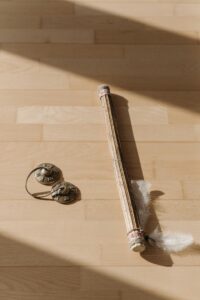 Tingsha bells and decorative stick on sunlit wooden floor.
