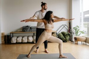 A woman practices yoga under the guidance of an instructor in a contemporary studio.